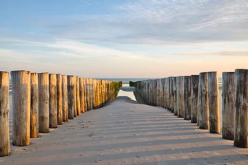 Photo sur Aluminium Mer du Nord, Pays-Bas Vue horizontale sur deux rangées de têtes de pieux menant vers la mer du Nord au coucher du soleil pendant le reflux en été. Paysage marin par une journée ensoleillée avec espace de copie.