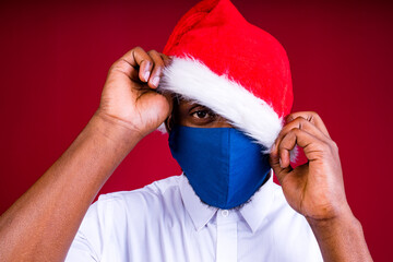 african american man in santas hat wearing mask in red studio background