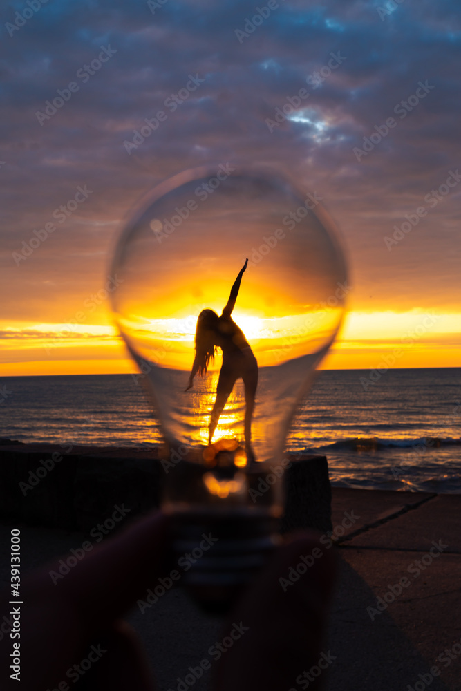 Wall mural a man holds up a lightbulb in front of a woman's silhouette with angled outstretched arms and body o