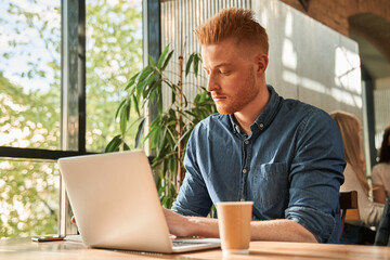 Man wearing jeans shirt being focused while sitting at the cafe and working