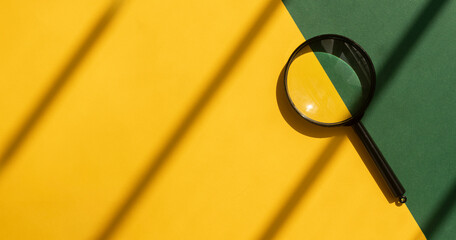 Magnifying glass over yellow and green background with copy space. Search tool on sunny bright...