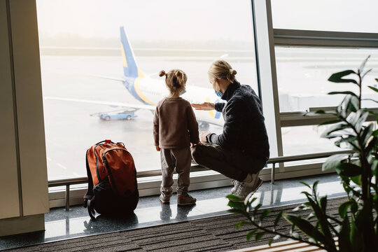 Man with girl ready to fly by airplane and the airport. Father and child looking though the lounge window on plane with backpack. Copy space, safe family travel in face mask during Covid-19 quarantine