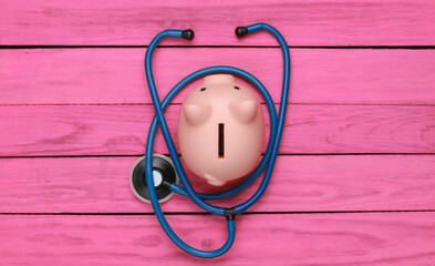 Medicine concept. Stethoscope with piggy bank on pink wooden background. Top view