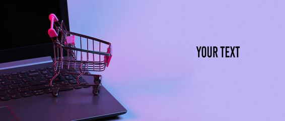 Mini supermarket trolley on laptop keyboard. Neon gradient red-blue, ultraviolet light. Online...