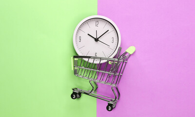 Shopping time. Supermarket trolley with clock on pink green background. Minimalism. Top view