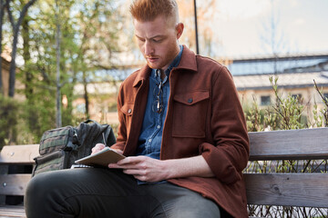 Fototapeta premium Man sitting at the bench and making some notes while working