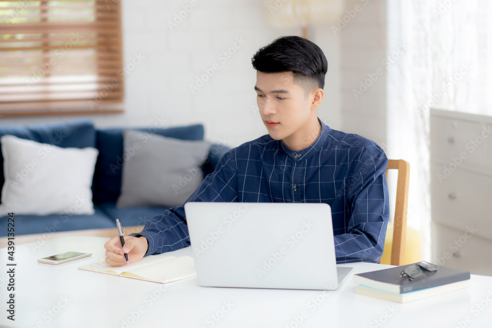 Poster young asian business man writing on notebook for planning working and using laptop computer on desk 
