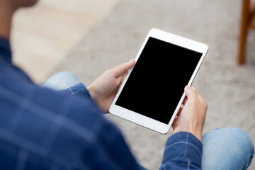Closeup young asian man sitting and using mockup of tablet computer with display blank screen on sofa at home, male holding digital tablet watch entertainment at living room, communication concept.