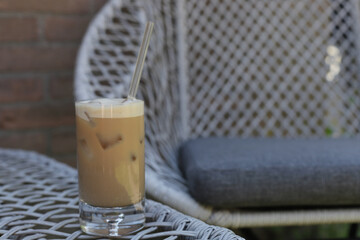 Ice coffee in glass cup with glass straw in back yard in garden.