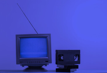 Antenna old-fashioned retro tv receiver and video cassettes in blue neon light. Retro media, entertainment 80s