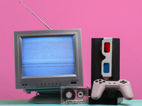 Retro media, entertainment 80s. Antenna old-fashioned retro tv receiver, anaglyph stereo glasses, audio and video cassette, gamepad on pink background.