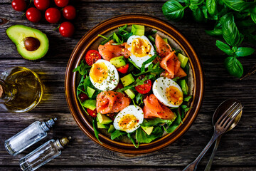 Salmon salad - smoked salmon, hard boiled eggs, avocado and green vegetables on wooden table
