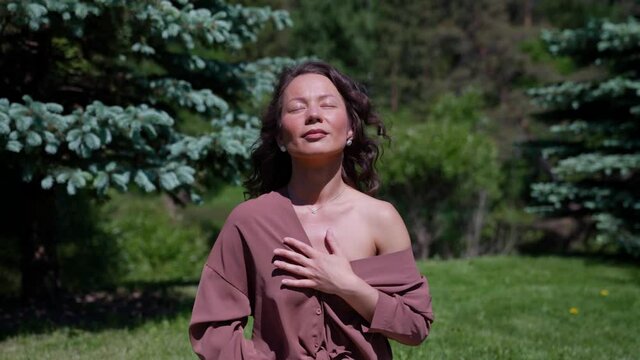 An Asian woman practices yoga and meditates in a lotus position in a park. Healthy girl sitting in the lotus position, meditating or practicing yoga in nature, outdoors