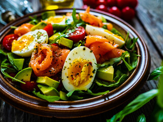 Salmon salad - smoked salmon, hard boiled eggs, avocado and green vegetables on wooden table
