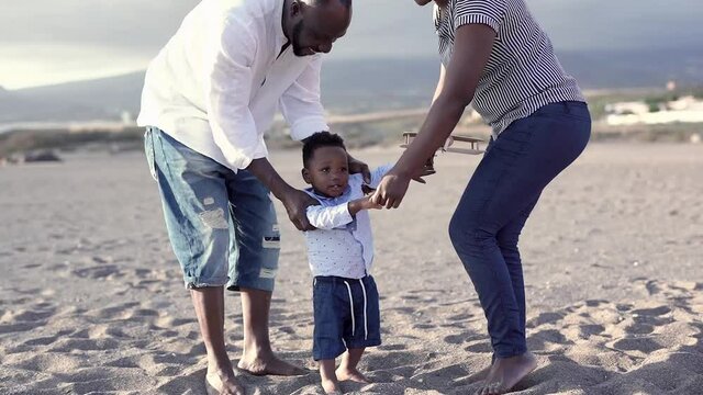 Black Family Enjoy Summer Vacation On The Beach - Mother, Father And Child Love - African Couple Dancing With Toddler Outdoor