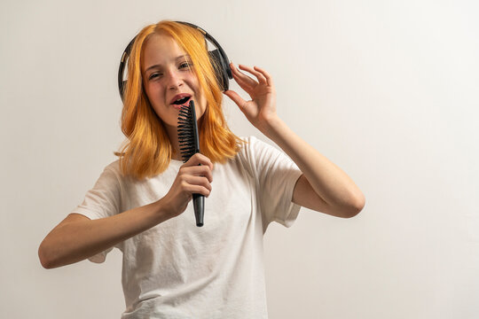 portrait of a teenage girl with red hair and in a white T-shirt singing in a hairbrush on a light background