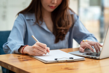 Close-up of businesswoman hand holding pen and taking notes using laptop keyboard sit at the office.