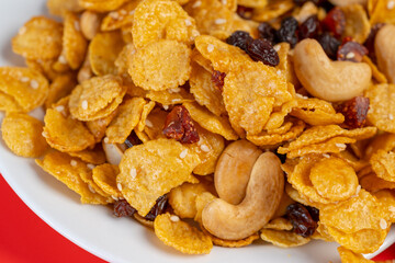 Cornflakes honey caramel homemade with grains, currant, cashew nut, dried strawberries and white sesame healthy food snack on a white plate close up and Macro copy space.