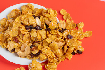 Cornflakes honey caramel homemade with grains, currant, cashew nut, dried strawberries and white sesame healthy food snack on a white plate close up and Macro copy space.