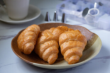 croissant on a brown plate next to a mug of milk on marble background
