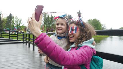 Cute girl and woman wear symbols usa national flag, happily talk in video conference by smartphone together, celebrating 4th of July in park. Activity technology lifestyle mobile phone use concept