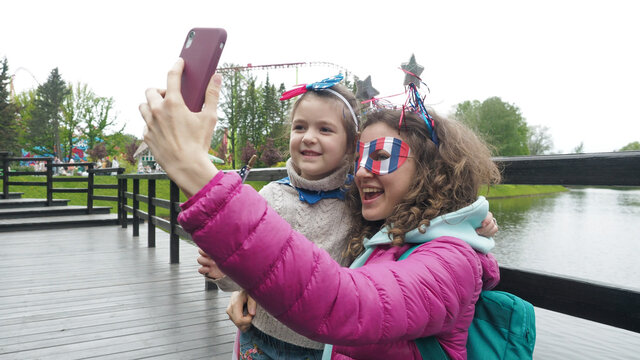 Cute girl and woman wear symbols usa national flag, happily talk in video conference by smartphone together, celebrating 4th of July in park. Activity technology lifestyle mobile phone use concept
