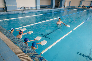 A group of boys and girls train and learn to swim in the pool with an instructor. Development of children's sports.