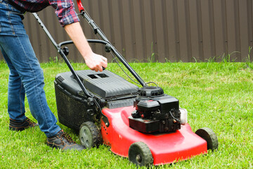 Lawn grass mowing. A man in blue jeans starts a gasoline lawn mower with his hand.