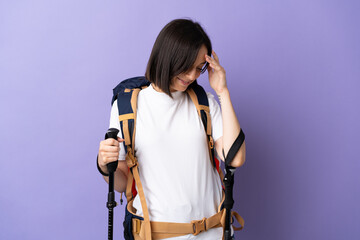 Young caucasian woman with backpack and trekking poles isolated on blue background laughing