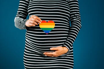 Closeup of pregnant woman holding a rainbow colored hearth against a black and white striped dress...