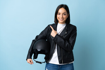 Woman holding a motorcycle helmet isolated on blue background pointing to the side to present a product