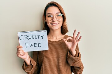 Young caucasian woman holding cruelty free message paper doing ok sign with fingers, smiling...