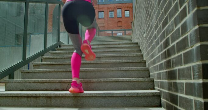 Beautiful blonde athlete running up the stairs on a sunny morning. Sporty young woman doing outdoor sports on sunny city streets. The girl in pink is having fun jogging
