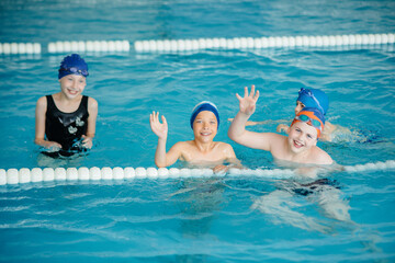 A group of boys and girls train and learn to swim in the pool with an instructor. Development of children's sports.