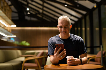 Portrait of man inside coffee shop at night using mobile phone