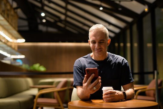 Portrait of man inside coffee shop at night using mobile phone - Powered by Adobe