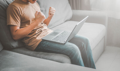 happy man with laptop sitting on sofa.Man with his arms up for having had some achievement.