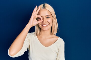 Beautiful blonde woman wearing casual sweater doing ok gesture with hand smiling, eye looking through fingers with happy face.