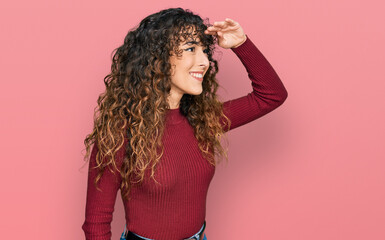 Young hispanic girl wearing casual clothes very happy and smiling looking far away with hand over...