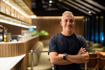 Portrait of man inside coffee shop at night smiling with arms crossed