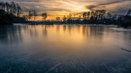 Fototapeta premium Dusk at winter evening on a frozen lake with silhouettes trees and reflection