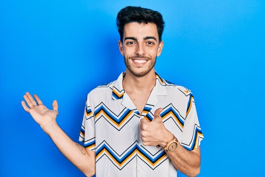 Young hispanic man wearing casual clothes showing palm hand and doing ok gesture with thumbs up, smiling happy and cheerful