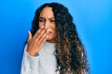 Young latin woman wearing casual clothes smelling something stinky and disgusting, intolerable...