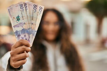 Young latin woman smiling happy holding colombia pesos banknotes at the city. - obrazy, fototapety, plakaty