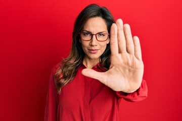 Young latin woman wearing casual clothes and glasses doing stop sing with palm of the hand. warning expression with negative and serious gesture on the face.