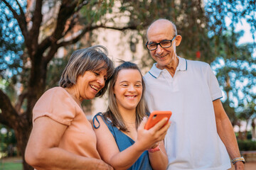 Latina family happy outdoors with daughter with down syndrome using smartphone. © Nexa