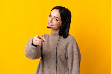 Young telemarketer woman isolated on yellow background pointing front with happy expression - obrazy, fototapety, plakaty