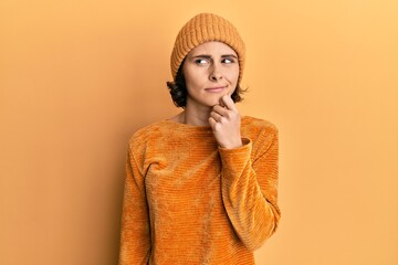 Young brunette woman wearing wool hat and winter sweater serious face thinking about question with...