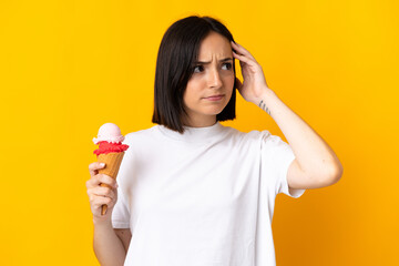 Young caucasian woman with a cornet ice cream isolated on yellow background having doubts and with...
