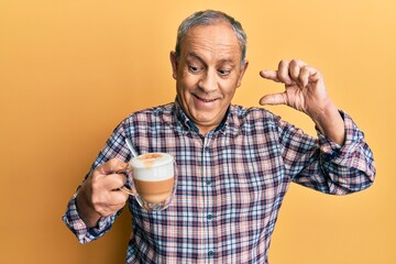 Handsome senior man with grey hair drinking a cup coffee smiling and confident gesturing with hand doing small size sign with fingers looking and the camera. measure concept.
